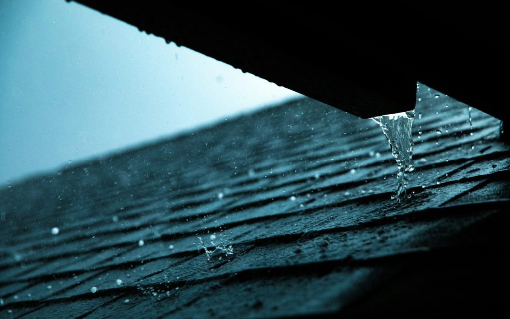 Rain pouring off the edge of a house roof during a storm